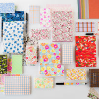 Collection of colorful stationery items including notebooks and planners with various patterns on a white background.